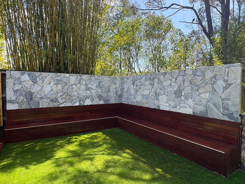 Stone wall feature with timber bench seating and artificial turf Brisbane